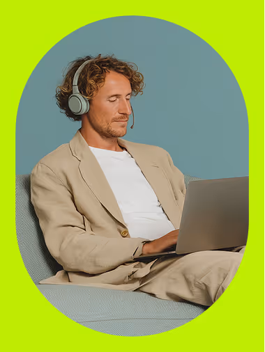 Un homme en tenue professionnelle, casque sur les oreilles, travaille sur un ordinateur portable dans un canapé, image d’un recrutement à distance efficace et de la flexibilité du travail moderne.